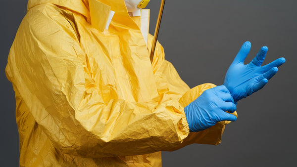 A figure in a yellow protective suit puts on a pair of blue protective gloves to support information about EN 374 Protective Gloves against chemicals and micro-organisms.