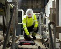 A worker in fluorescent yellow overall and white helmet kneels to work on the floor of a staircase to support our guide on ANSI/ISEA 107 on High Visibility Safety Apparel.