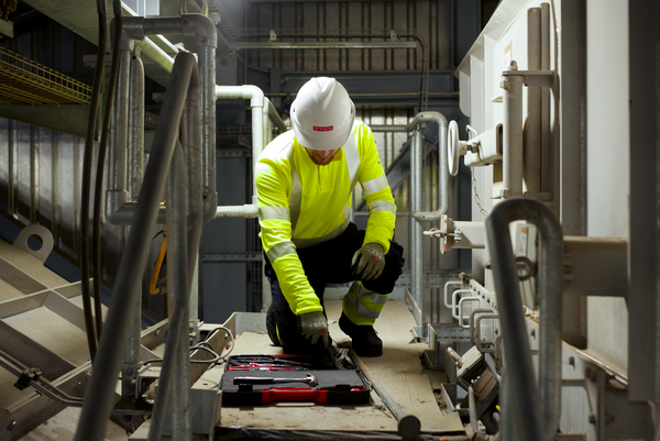 A worker in fluorescent yellow overall and white helmet kneels to work on the floor of a staircase to support our guide on ANSI/ISEA 107 on High Visibility Safety Apparel.