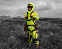 A man stands in a field wearing fluorescent yellow trousers, jacket and hood to support our guide about EN 20471: High Visibility Clothing