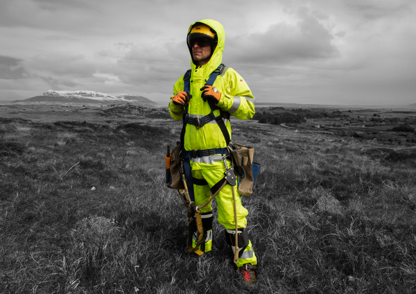 A man stands in a field wearing fluorescent yellow trousers, jacket and hood to support our guide about EN 20471: High Visibility Clothing
