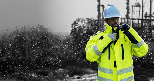 A man in a white helmet and thick fluorescent winter jacket stands in front of a stark winter landscape to support information about EN342, Protective clothing - Ensembles and garments for protection against cold 