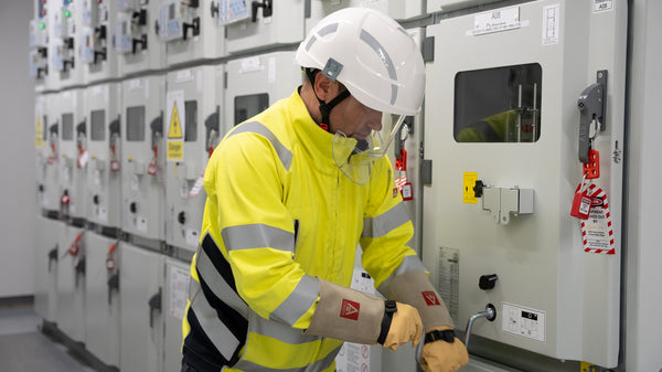 A man in a white helmet and fluorescent yellow works on a large electrical device. Used to support information about NFPA 70 E